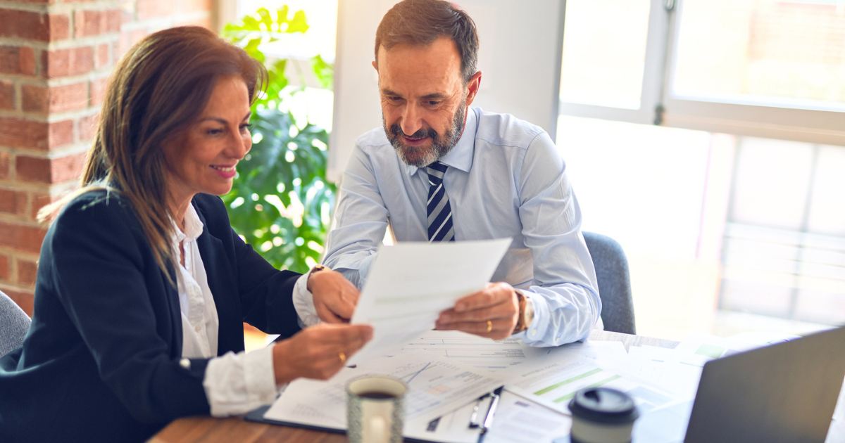 Business advisor and client reviewing tax documents together in office, discussing deductible expenses and tax planning strategies for business owners
