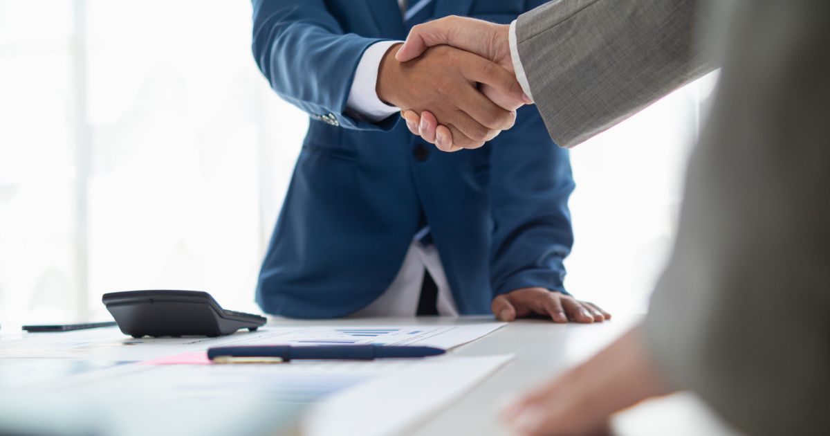 Professionals shaking hands over financial documents, symbolizing choosing the right financial advisor.